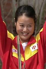 Photographie de Zhang Shan en tenue sportive rouge et jaune, souriante, les bras levés. On voit les cordons de sa médaille d'or autour de son cou.