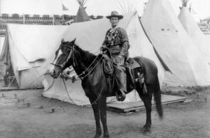 Photographie de Calamity Jane montée à cheval, devant des tentes claires