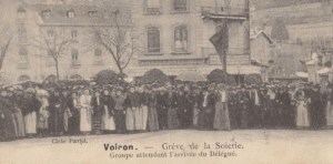 Photographie de la grève de Voiron montrant la foule des grévistes en train d'attendre sur une place, devant des bâtiments. La légende dit : "Voirin - grève de la scierie. Groupe attendant l'arrivée des délégués".