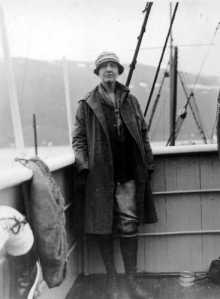 Photographie en noir et blanc de Louise Boyd debout sur son bateau, appuyée contre la balustrade