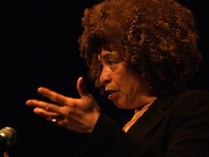 Photographie d'Angela Davis en train de délivrer un discours, de profil, une main levée à côté de son visage
