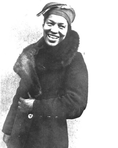 Photographie en noir et blanc de Zora Neale Hurston souriante en manteau d'hiver