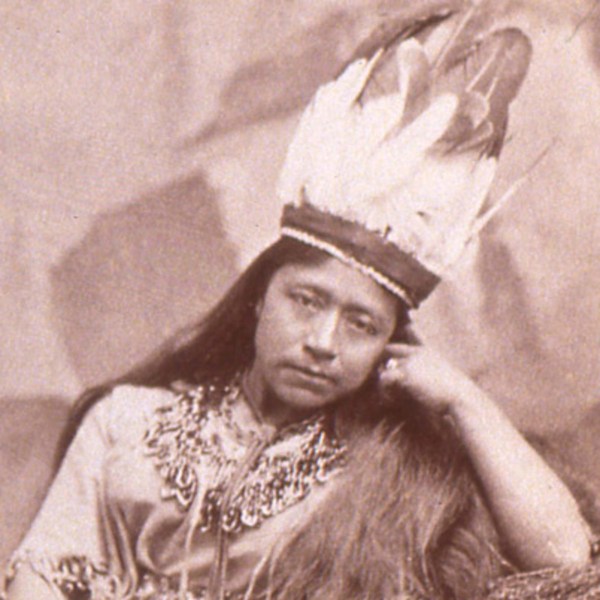 Cette photoghraphie montre Sarah Winnemucca, portant des habits et une coiffe de plumes païutes. Accoudée, elle a le visage appuyé contre sa main gauche et regarde l'objectif.