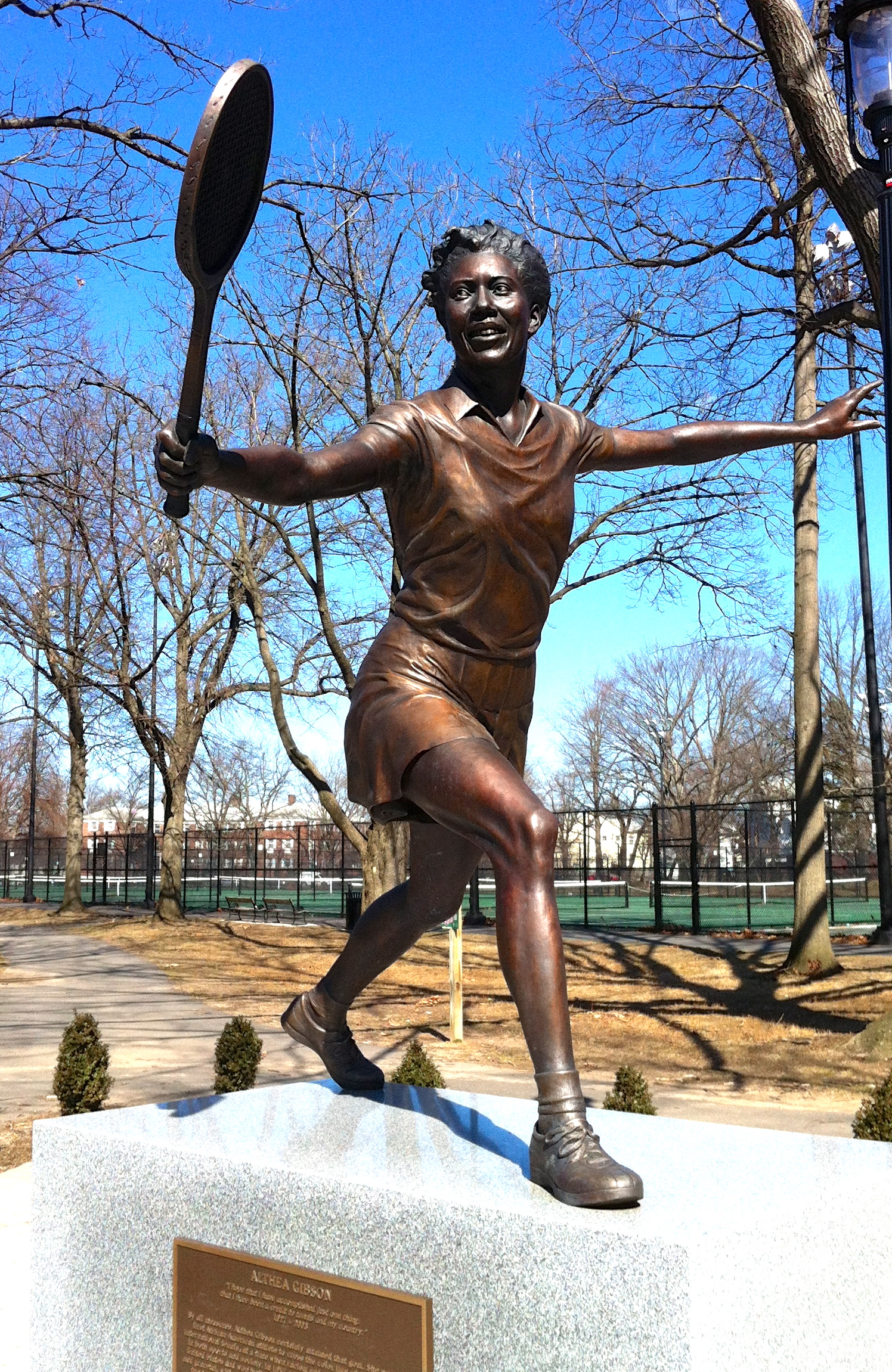 Cette photographie montre une statue d'Althea Gibson. Elle est représentée raquette à la main, en mouvement, bras tendus, en train de jouer au tennis.