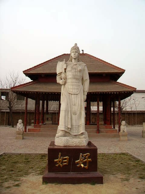 Cette photographie montre une statue de Fu Hao à Yinxu. Fu Hao est représentée debout, en habits militaires, coiffée d'un casque et tenant une hache à la main.