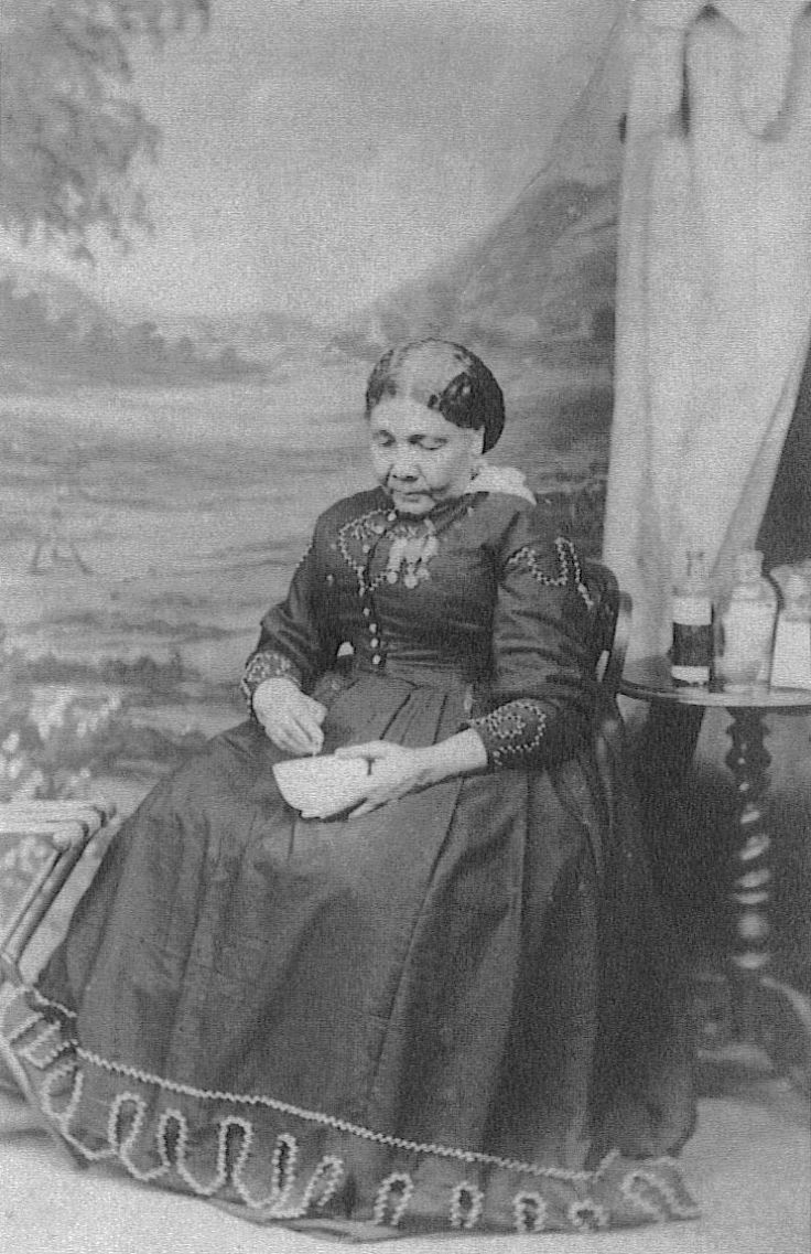 Cette photographie montre Mary Seacole assise sur une chaise. Elle porte une robe longue à la jupe évasée recouvrant jusqu'à ses pieds. Ses mains reposent sur ses cuisses, sa main droite tient un bol. Cheveux soigneusement coiffés, elle regarde vers le bas. Derrière elle, on aperçoit un guéridon avec plusieurs flacons.