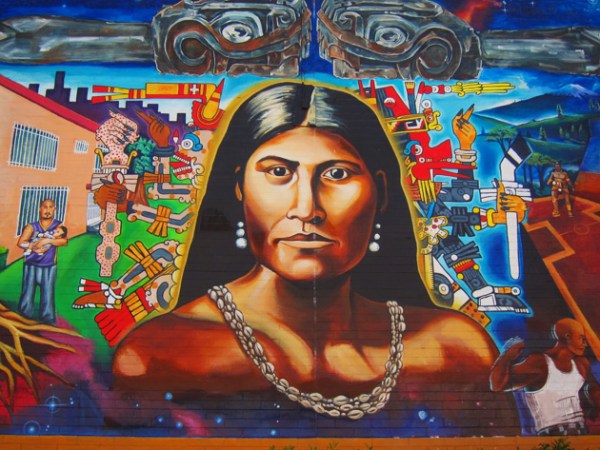 Cette photographie montre une fresque murale représentant Toypurina. Elle a les cheveux lâchés et porte des boucles d'oreille et un collier de coquillages.