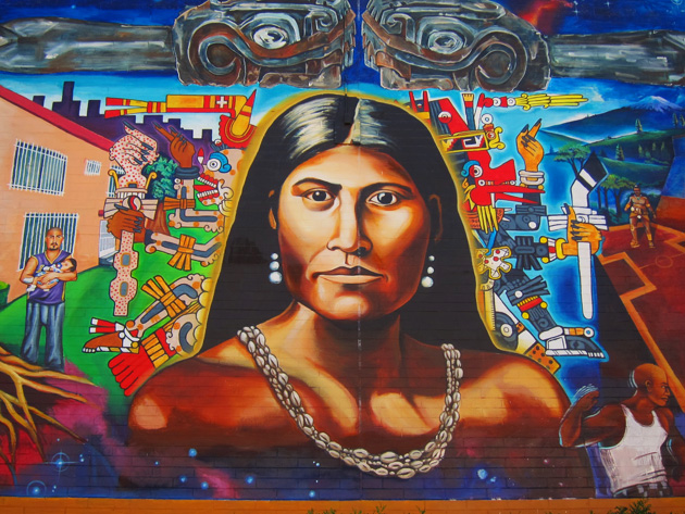 Cette photographie montre une fresque murale représentant Toypurina. Elle a les cheveux lâchés et porte des boucles d'oreille et un collier de coquillages.