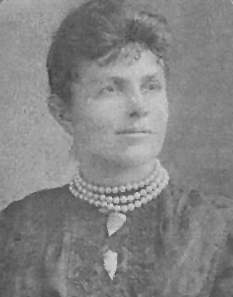 Cette photographie en noir et blanc montre une femme de profil, portant une veste sombre et un collier ras-du-cou à trois rangs de perles blanches. Il pourrait s'agir de Maria Beasley