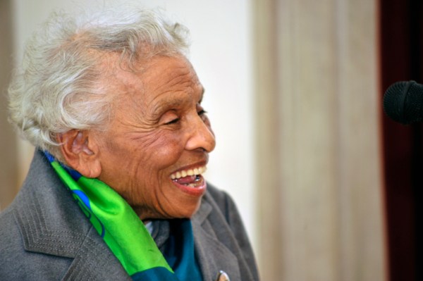 Cette photographie montre Olivia Hooker à l'âge de 97 ans. Ses cheveux blancs sont courts. Elle porte une veste grise et un foulard vert et bleu. Regardant vers la droite, elle a un large sourire.