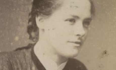 Cette image est une photographie en noir et blanc de Maggie Hugues, membre des Forty Thieves et bras droit d'Alice Diamond. Elle regarde vers la droite avec un demi-sourire et porte ses cheveux attachés en arrière.