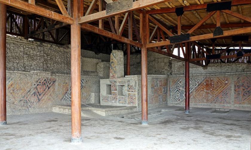 Cette photographie montre une salle funéraire de la huaca Cao Viejo, dans le site archéologique El Brujo au Pérou. Les murs anciens sont couverts de fresques géométriques colorées. Un plafond de bois récent a été créé, supporté par des poutres de bois.