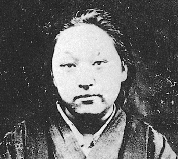 Cette photographie en noir et blanc montre Fukuda Hideko. Elle porte des vêtements traditionnels japonais et ses cheveux sont retenus en arrière.