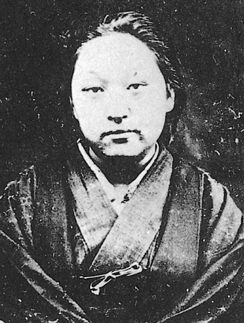 Cette photographie en noir et blanc montre Fukuda Hideko. Elle porte des vêtements traditionnels japonais et ses cheveux sont retenus en arrière.