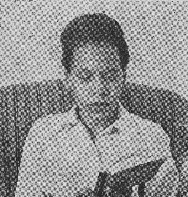 Cette photographie en noir et blanc montre Virginia Brindis de Salas, assise sur un canapé, absorbée dans la lecture d'un livre ouvert entre ses mains. Elle porte une chemise claire.