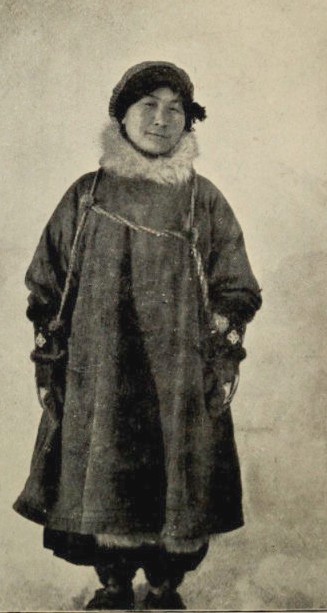 Cette photographie en noir et blanc montre Ada Blackjack en pied. Elle porte un manteau épais, de la fourrure autour du cou et un manteau.