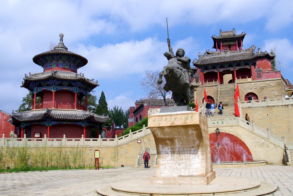 Cette photographie montre le Palais temporaire de Li Zicheng dans le Shaanxi. Au premier plan, une statue d'un combattant à cheval. Derrière, des escaliers montent vers deux bâtiments rouges aux toits sombres.