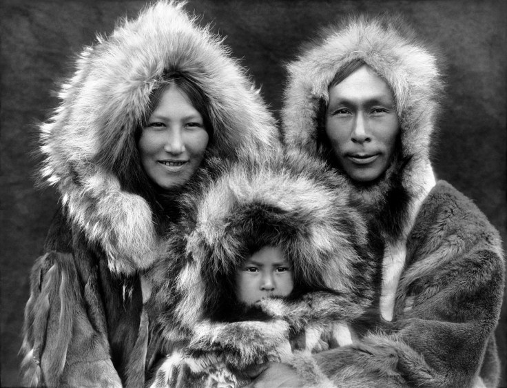 Cette photographie en noir et blanc montre une famille inupiat, en Alaska (en 1929). On y voit une femme à gauche, un homme à droite et un jeune enfant entre les deux. Tous les trois portent des capuches de fourrure et des vêtements chauds.