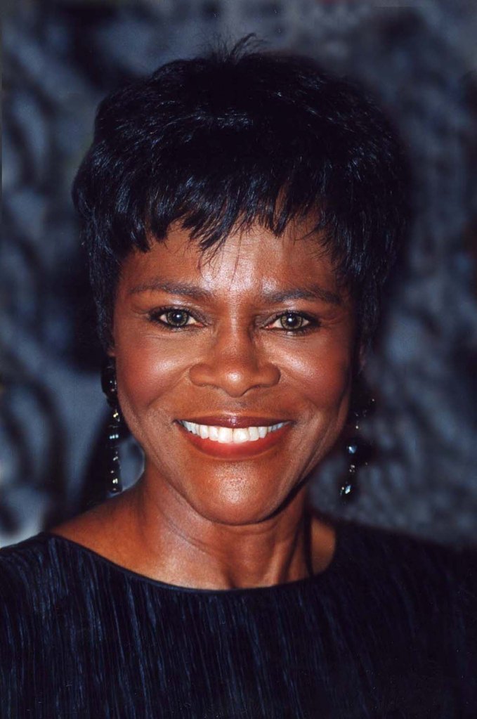 Cette image est un portrait de Cicely Tyson. Elle porte un haut sombre et de longues boucles d'oreille. Ses cheveux sont courts. Elle sourit.