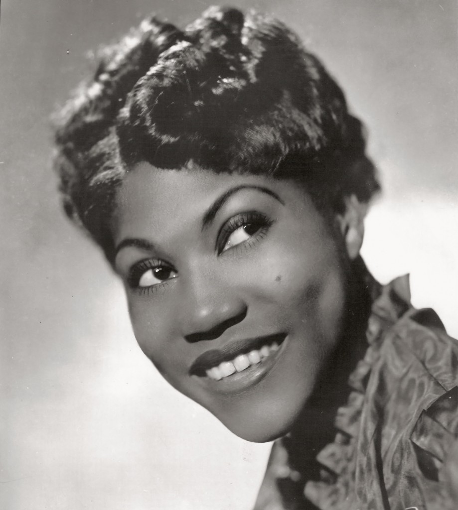 Cette photographie en noir et blanc est un portrait de Rosetta Tharpe en 1938, centré sur le visage. Elle a un large sourire et regarde en haut à droite. 