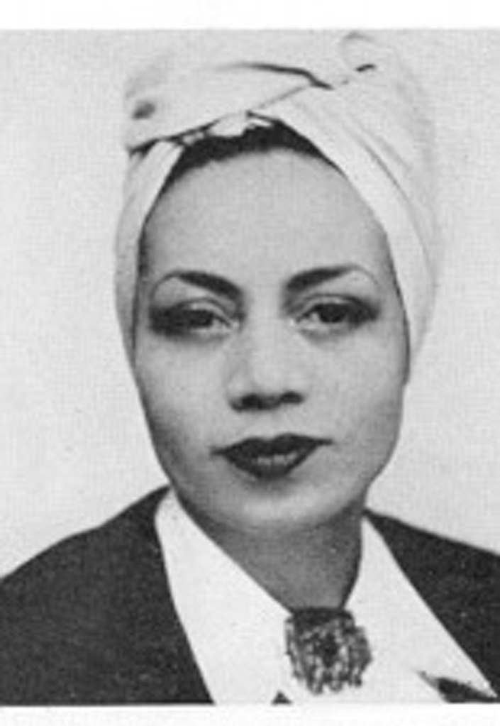 Cette image est un portrait en noir et blandnc de Jane Vialle, centré sur le visage. Elle a les cheveux retenus dans un foulard et sourit à demi.